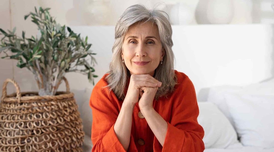 Mulher madura com expressão tranquila, sentada num ambiente luminoso e natural, simbolizando equilíbrio e bem-estar durante a menopausa.
