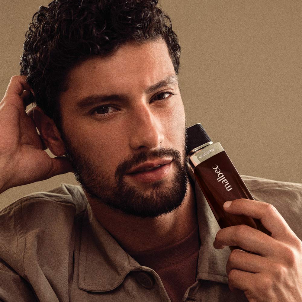 Modelo masculino a segurar o perfume Malbec Eau de Toilette oBoticário.