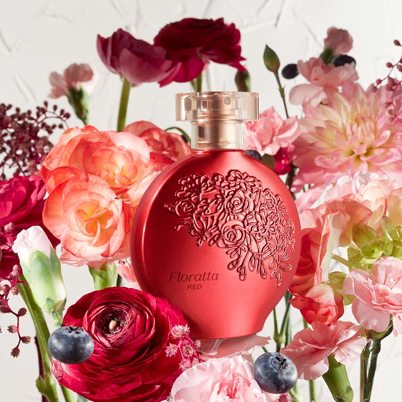 Perfume Floratta Red 75ml do Boticário, frasco vermelho com relevo floral, colocado entre flores vermelhas e rosas e pequenos frutos, em ambiente luminoso.