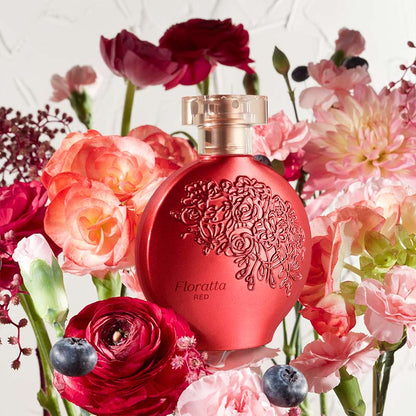 Perfume Floratta Red 75ml do Boticário, frasco vermelho com relevo floral, colocado entre flores vermelhas e rosas e pequenos frutos, em ambiente luminoso.