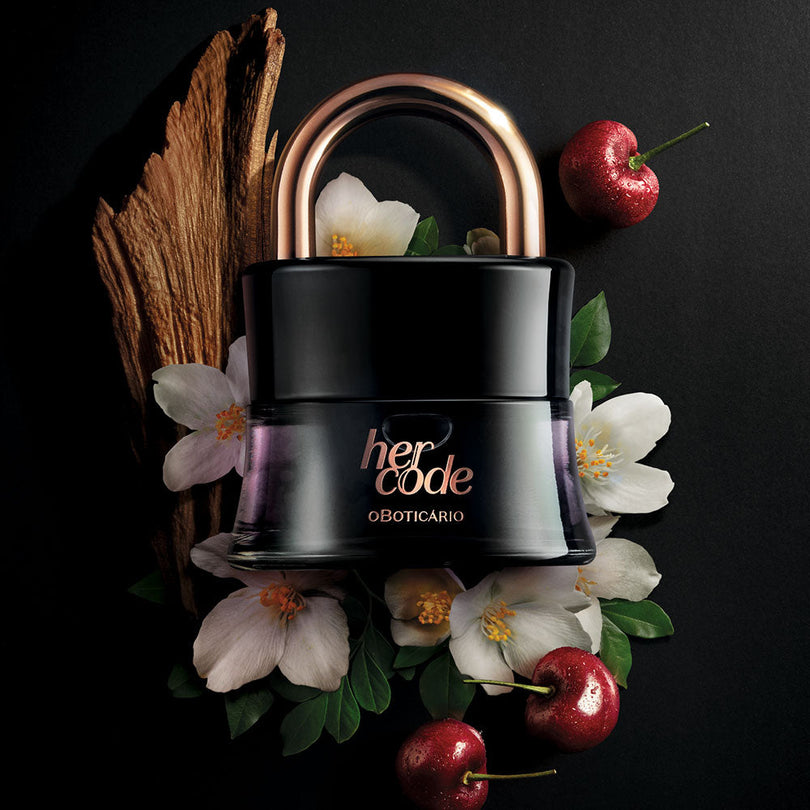 Perfume Her Code 50ml do Boticário, frasco em forma de cadeado preto com detalhe rose gold, colocado sobre flores brancas, cerejas e madeira em fundo escuro.