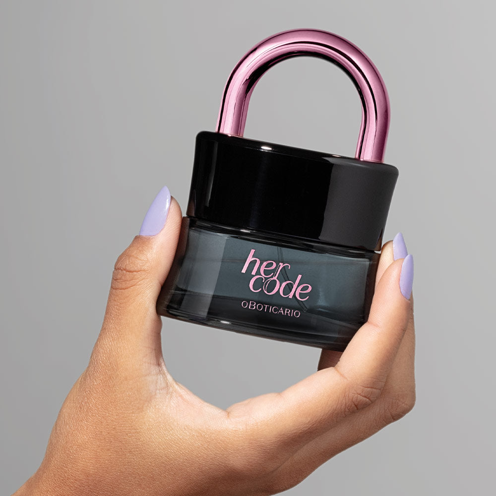 Frasco do perfume Her Code Touch 50ml do Boticário em forma de cadeado com arco rosa metálico, segurado por uma mão com unhas lilás.