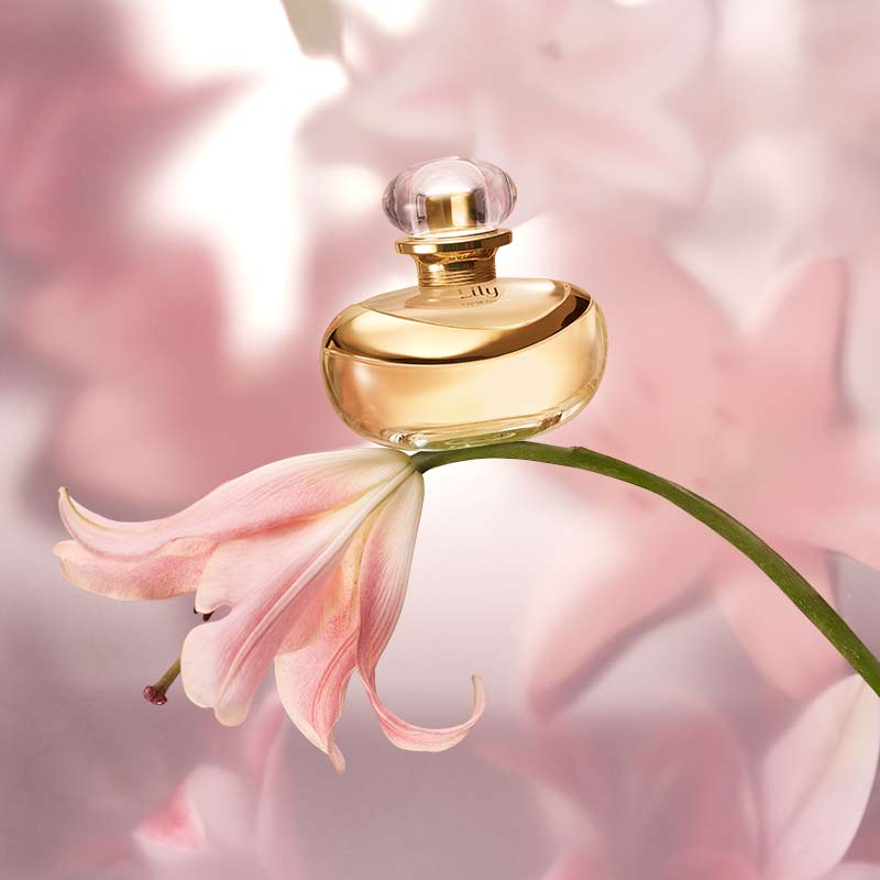 Perfume Lily 75ml do Boticário pousado sobre uma flor rosa, com fundo difuso em tons suaves, destacando o frasco dourado.