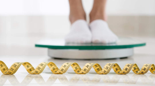 Pessoa a pesar-se numa balança com fita métrica à frente, simbolizando emagrecimento saudável.